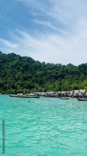 Sea gypsies wooden frishing boat on turquoise water n calm ocean wave at Moken or Morgan Village in Surin island with mountain n rain-forest in tropical summer sunlight on clear blue sky n white cloud