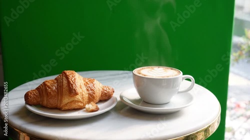 Cozy cafe window seat with steaming cappuccino latte art golden croissant on marble table green screen backdrop hot coffee breakfast pastry steam white cup saucer fresh morning ambiance