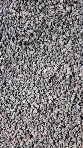 Top view of a textured surface featuring small, gray crushed gravel stones and pebbles, ideal for use as a natural background or construction material texture.