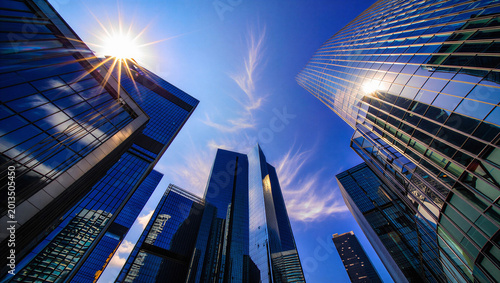 Bild auf Leinwand Low Angle View of Glass Skyscrapers and Blue Sky with Bright Sun Flares