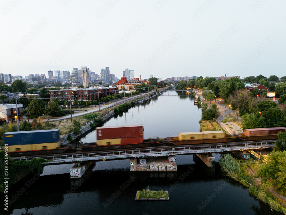Obraz premium Freight train crossing Lachine Canal at dusk with Montreal skyline and urban waterfront, Quebec, Canada. g.