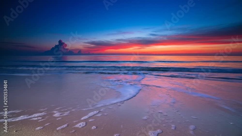 Waves wash onto sandy beach at vibrant sunset with orange clouds and blue sky