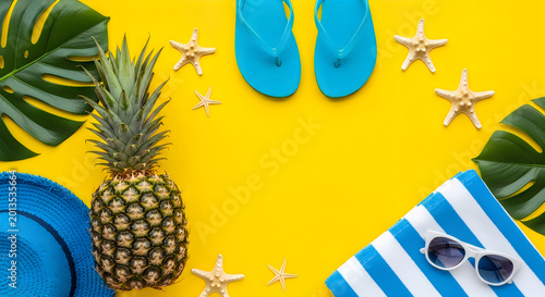 Summer vacation concept with pineapple blue flip flops starfish and tropical leaves on a bright yellow background