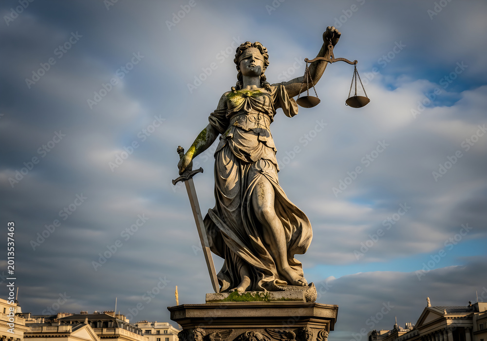 Obraz premium Statue of lady justice holding a sword and scales of balance against a dramatic cloudy sky in the city center