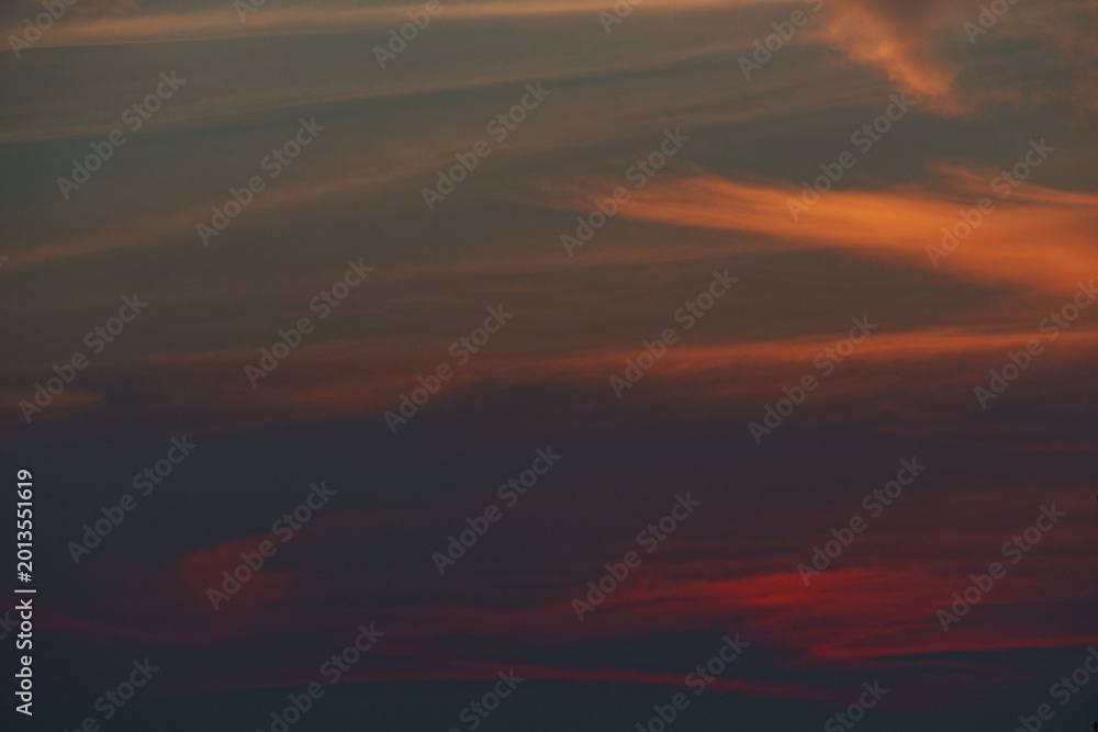 Fototapeta premium Intense fiery sunset clouds with dark blue sky during evening transition. Dramatic weather and atmosphere for creative use.
