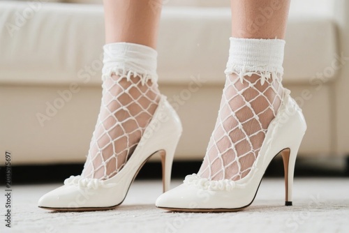 White high-heeled shoes with fishnet socks and lace trim worn by a person indoors