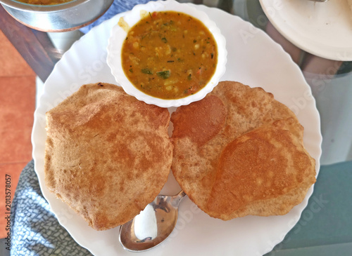 Crispy puffed pooris served alongside flavorful vegetable curry in white serving bowl.