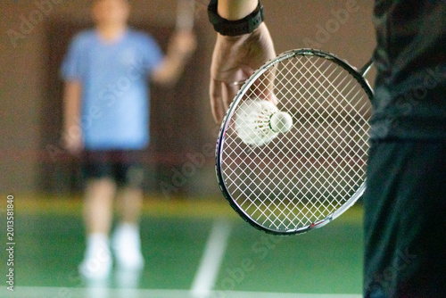 Badminton player holds racket and white cream shuttlecock in front of the net before serving it to another side of the court.