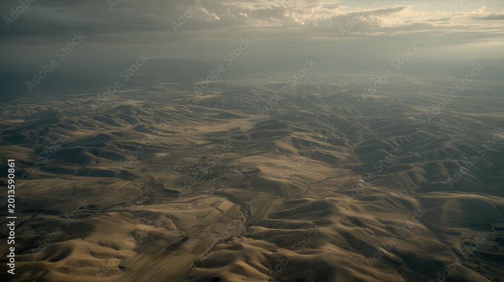 Fototapeta premium Expansive arid terrain features undulating hills and distant fields, stretching to the horizon under a dramatic, cloudy sky, creating a feeling of desolation and remote wilderness
