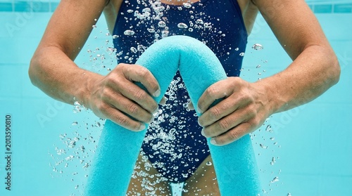 Close-up of hands holding a blue foam pool noodle underwater in a swimming pool with rising bubbles, water aerobics and fitness concept
