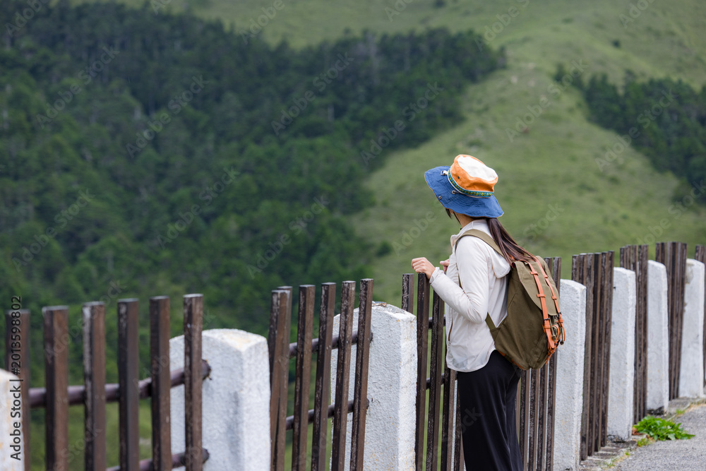 Obraz premium Hiker woman standing at wooden fence enjoying mountain scenery