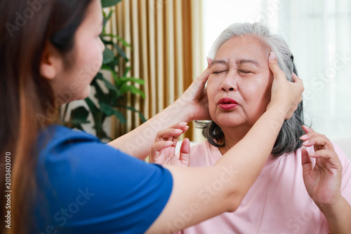 Professional nurse checking a senior patient for headache and providing comfort. Specialized geriatric home care service.