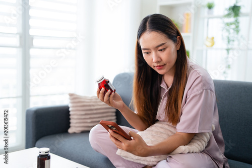 A woman is holding a bottle of medicine and using her smartphone to search online for medication instructions.