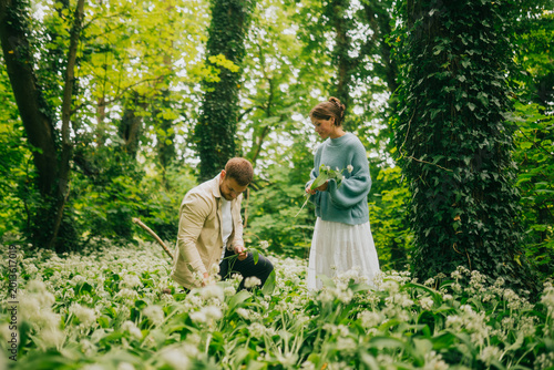 A couple gathers wild garlic in a vibrant woodland setting