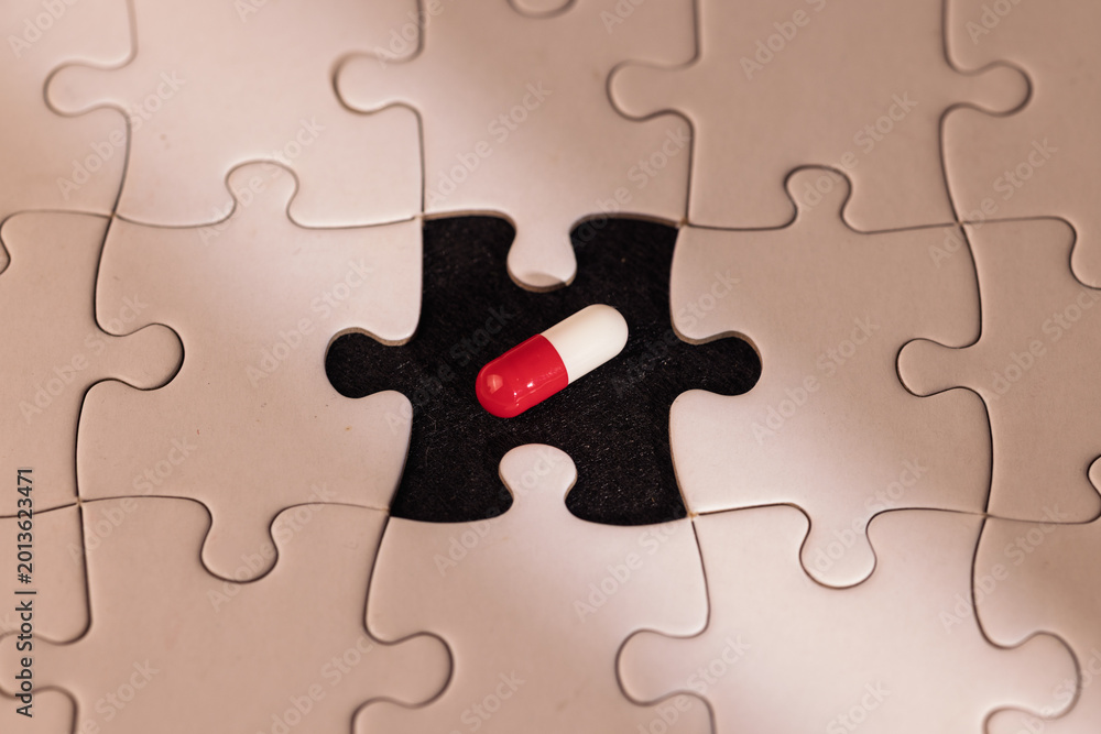 Fototapeta premium Detailed view of a white puzzle missing one piece with a glowing pill in the empty space under a light ray on a deep black backdrop.