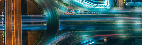 Aerial night view of modern highway interchange with dynamic light trails representing sustainable transportation, EV mobility, smart city growth, ESG investment, and futuristic urban infrastructure.