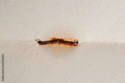 Obraz na plátně Close-up of a rusty staple holding together aged, textured paper with a crease