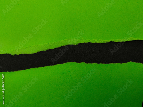 Two pieces of vibrant green paper are torn to reveal a dark, black textured space between them