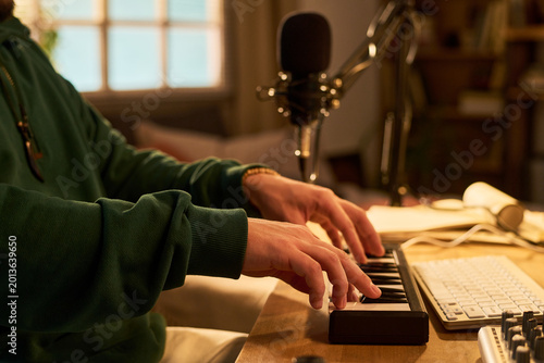 Fotografia Young adult man composing music on MIDI keyboard beside microphone and computer workstation, creating audio content