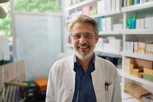 Happy mature pharmacist at work looking at camera.