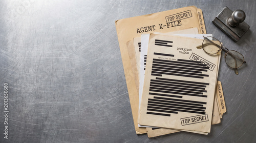Mysterious files and documents related to the secret agent's investigations and a pair of eyeglasses on a metal surface
