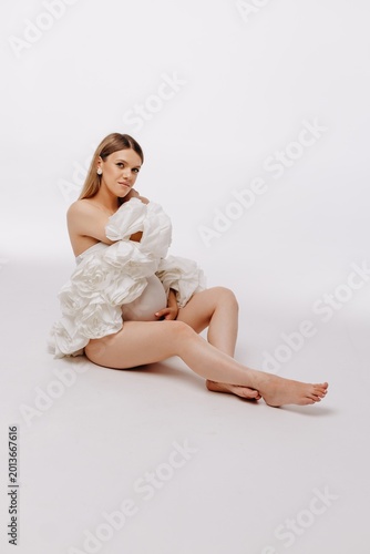 Photography Pregnant woman in white floral maternity gown sitting in studio, elegant portrai