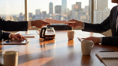 Fotografie Two business professionals exchanging important documents and contracts across a conference table