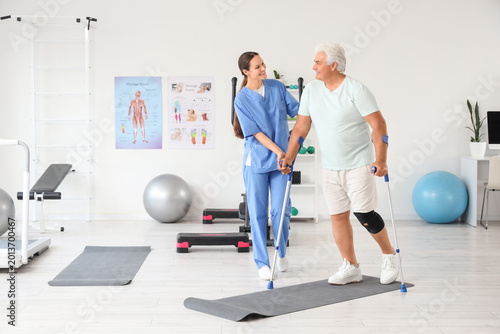 Foto Senior man with crutches and therapist walking in rehabilitation center