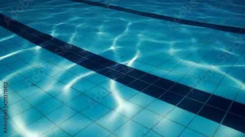 Clear swimming pool water with tile pattern and sunlight reflections  