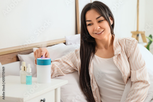 Foto Young woman turning air humidifier on table in bedroom