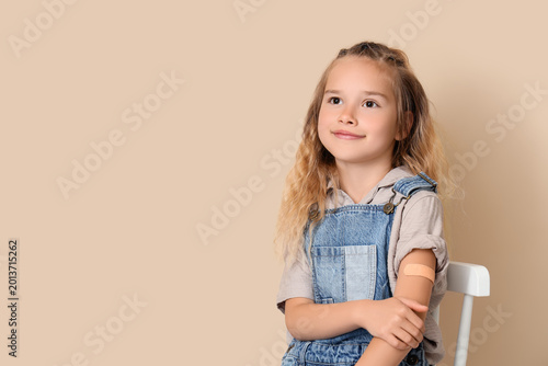 Little girl with applied patch after vaccination on beige background