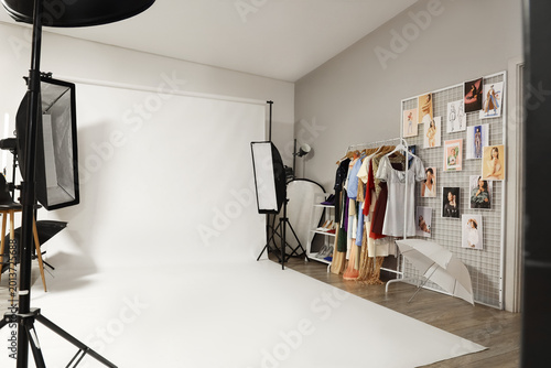 Interior of modern photo studio with professional equipment, clothes rack and...