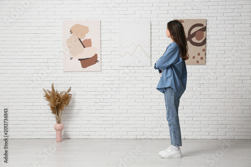 Foto Young woman looking at paintings on white brick wall in art gallery