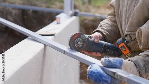 Site Worker Finishing Metal Rail With Grinder Wheel, Gloved Hands Smoothing Surface Near Concrete Edge, Sparks And Rotating Disc Visible, Quality Control And Alignment For Installation
