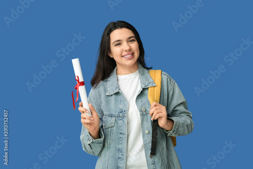 Happy smiling female student with backpack and diploma on blue background