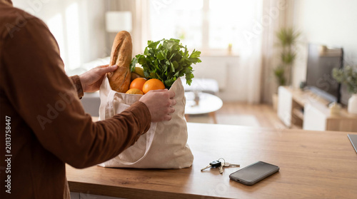 Bild auf Leinwand A person unpacks fresh groceries from a reusable cloth bag onto a kitchen counter