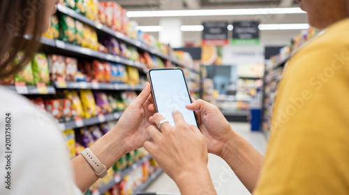 Tableau sur toile Two people in a supermarket aisle holding a modern smartphone with a blank white screen, shopping