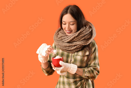Beautiful young Asian woman in warm scarf holding cup of cocoa with marshmall...