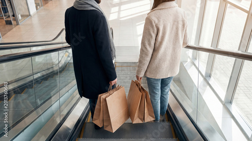 Photos Couple with shopping bags on an escalator moving down in a bright and modern shopping mall