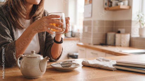 Photos Woman's hands holding a clear glass of herbal tea at a kitchen table, symbolizing peace and wellness indoors