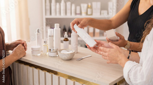 Obraz na płótnie Two women discussing skincare products at a beauty counter, holding cosmetic bottles and packaging for sale
