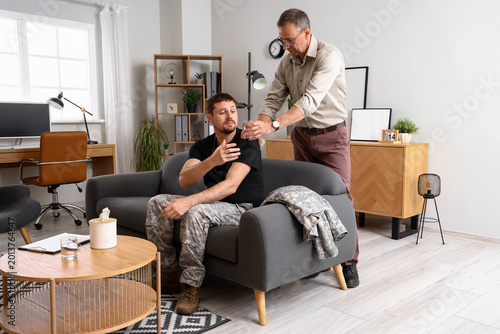 Mature psychologist giving glass of water to soldier in office