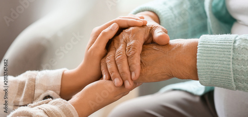 Senior woman with daughter holding hands at home, closeup