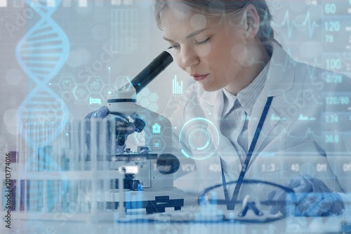 Female scientist looking through microscope in laboratory. DNA research techn...