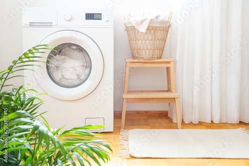 Washing machine, basket with laundry and green houseplant in laundry room
