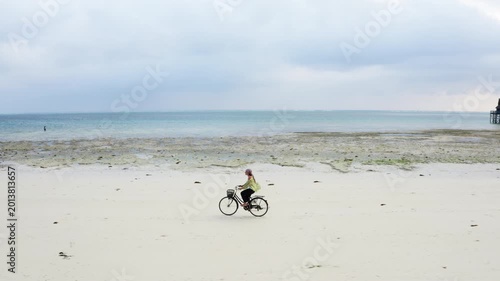 4K footage of young woman riding on bicycle along beautiful packed damp sand beach. Spending time outside, sports, leisure activities concept.. Environment, healthy lifestyle, outdoors concept.
