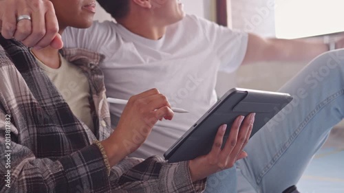 A couple sits cozily on a couch, engrossed in a tablet, their relaxed postures. The room's soft lighting and casual attire reflect a moment of bonding.