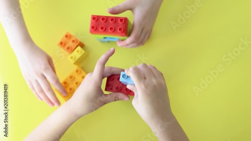 Close-up of two kids' hands as they play with a construction set, carefully assembling colorful pieces. Their teamwork and creativity shine as they build imaginative structures together.