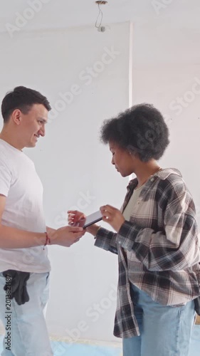 A young couple collaborates on a digital tablet discussing home renovation plans. The modern, minimalistic room suggests they're focused on interior design or layout changes.