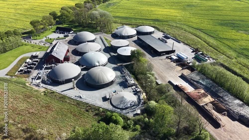 Vertical aerial perspective of biogas tanks, storage sheds, and organic matter piles at a renewable energy site in Denmark.